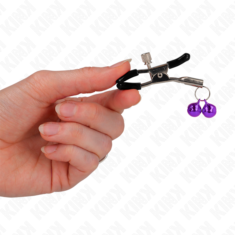 Pinzas para pezones KINK NIPPLE GRIP con doble campanilla violeta, 6 cm, en uso en una mano.